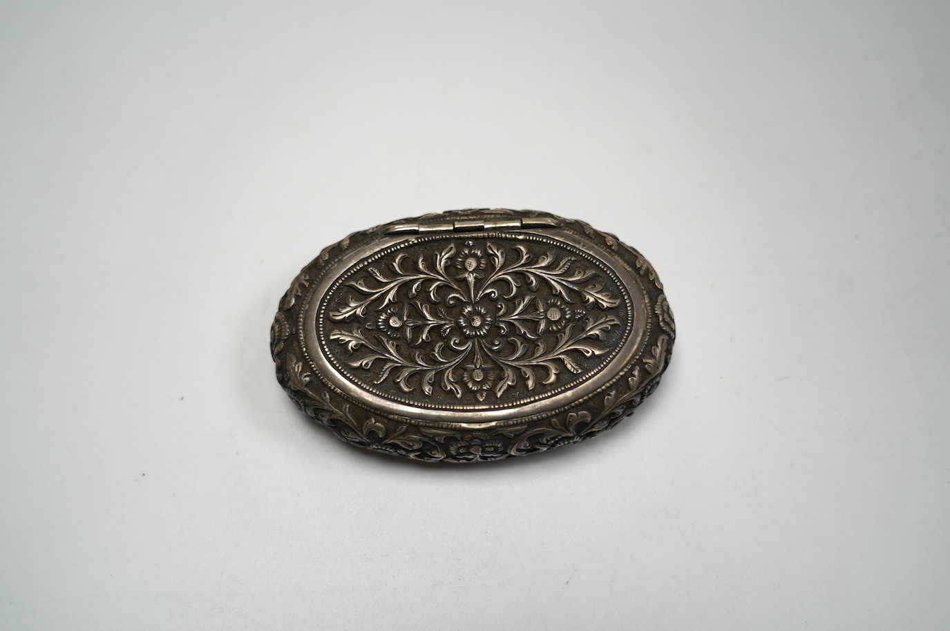 An Indian embossed white metal oval tobacco box, 97mm. Condition - poor to fair